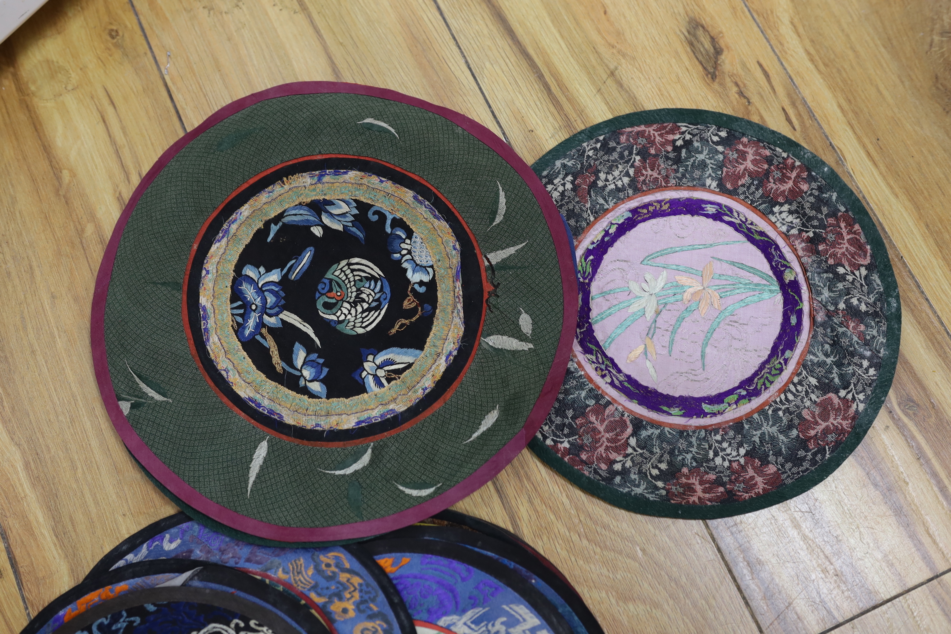 Forty two Chinese embroidered circular mats with damask borders, largest 25cm in diameter